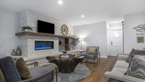 A modern living room with a stone fireplace, a flat-screen TV, and a wooden coffee table.