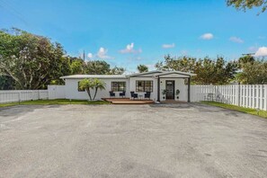 A single-story house with a front porch, a small patio, and a fenced yard. - Bungalow! Hot TUB! Games! 10 min to Beach! (Palm Beach County)