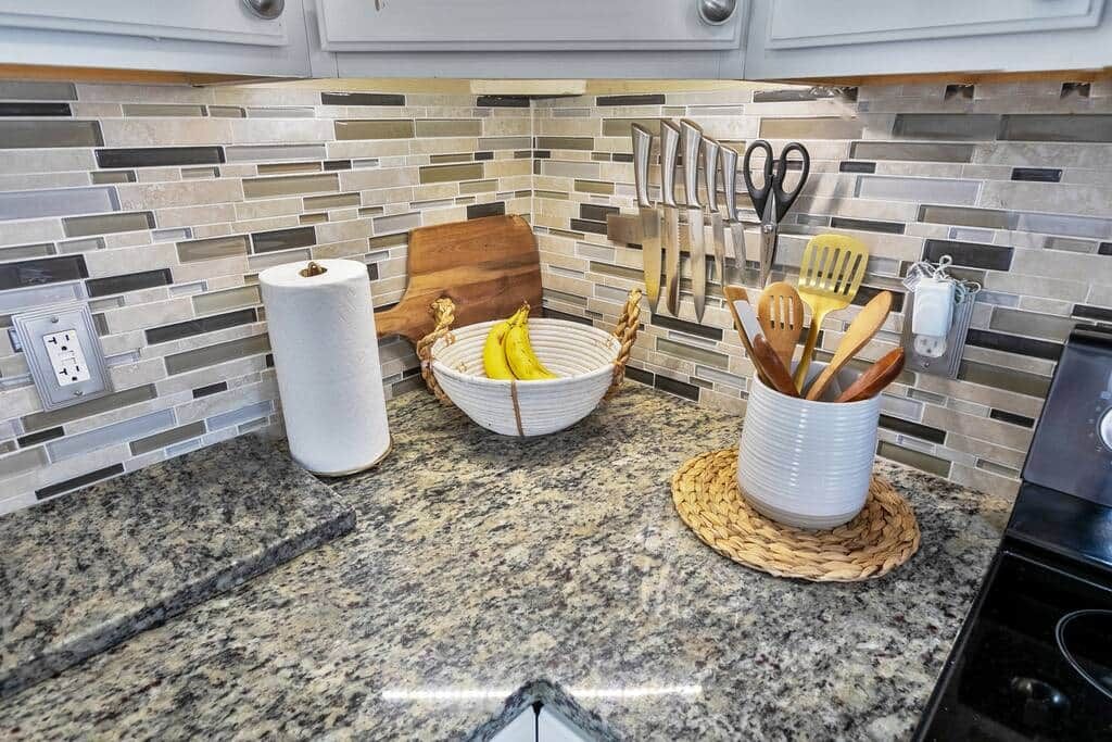 Una cucina con piani in granito, un tagliere di legno, una ciotola con banane e un portauoviglie.