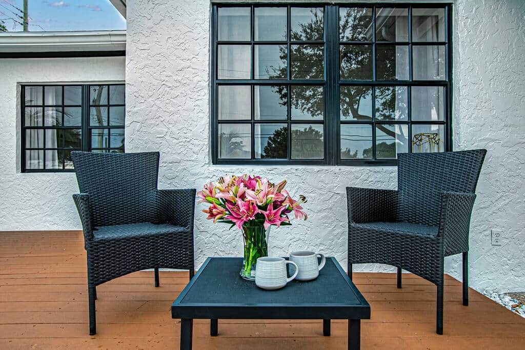 Two wicker chairs, a small table, and a vase of flowers on a wooden deck.