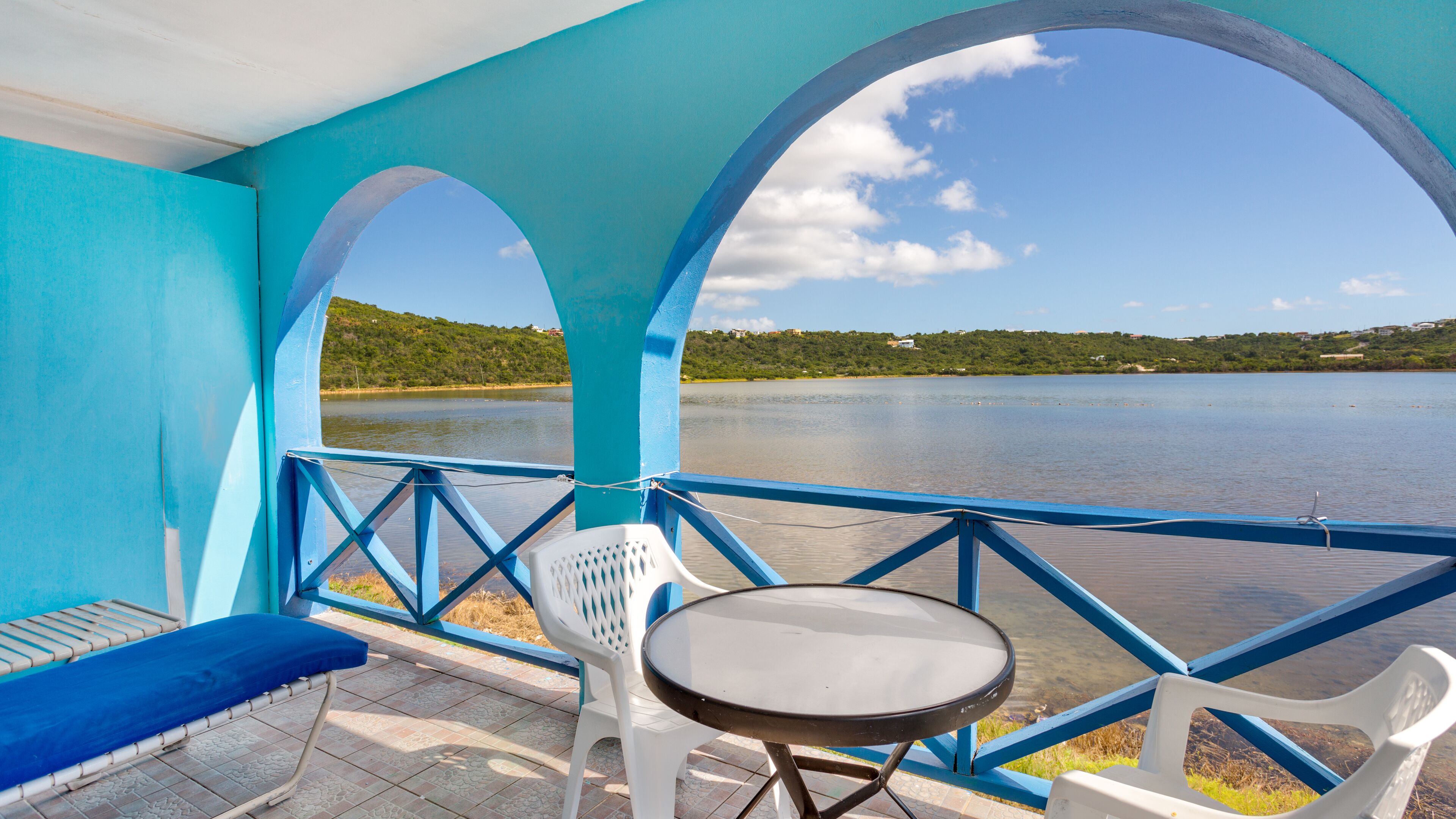 Un espace extérieur abrité, avec une table et des chaises, offrant une vue sur un lac paisible et une colline verdoyante.