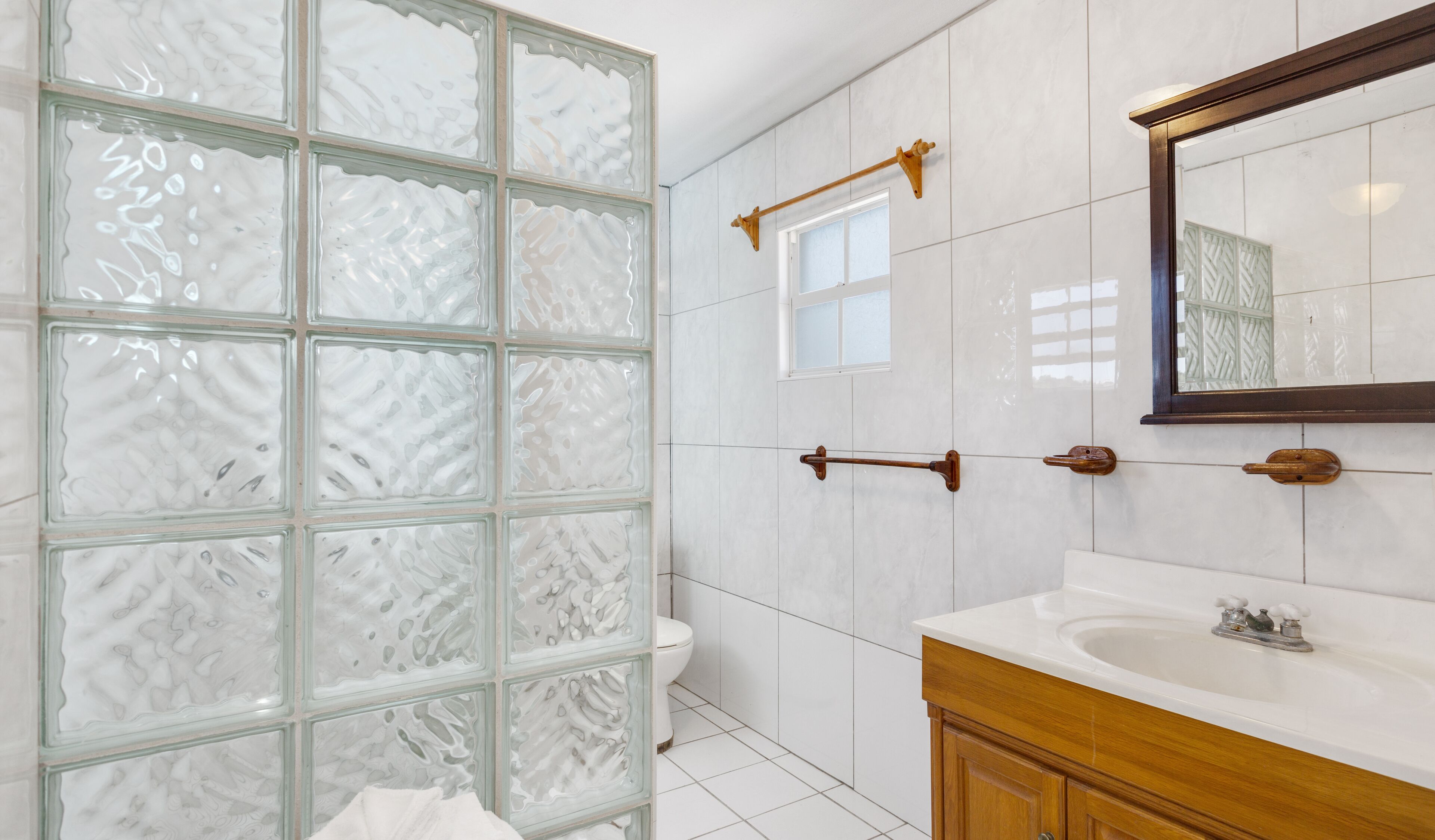 A bathroom with a glass shower enclosure, white tiles, a wooden vanity, and a mirror.