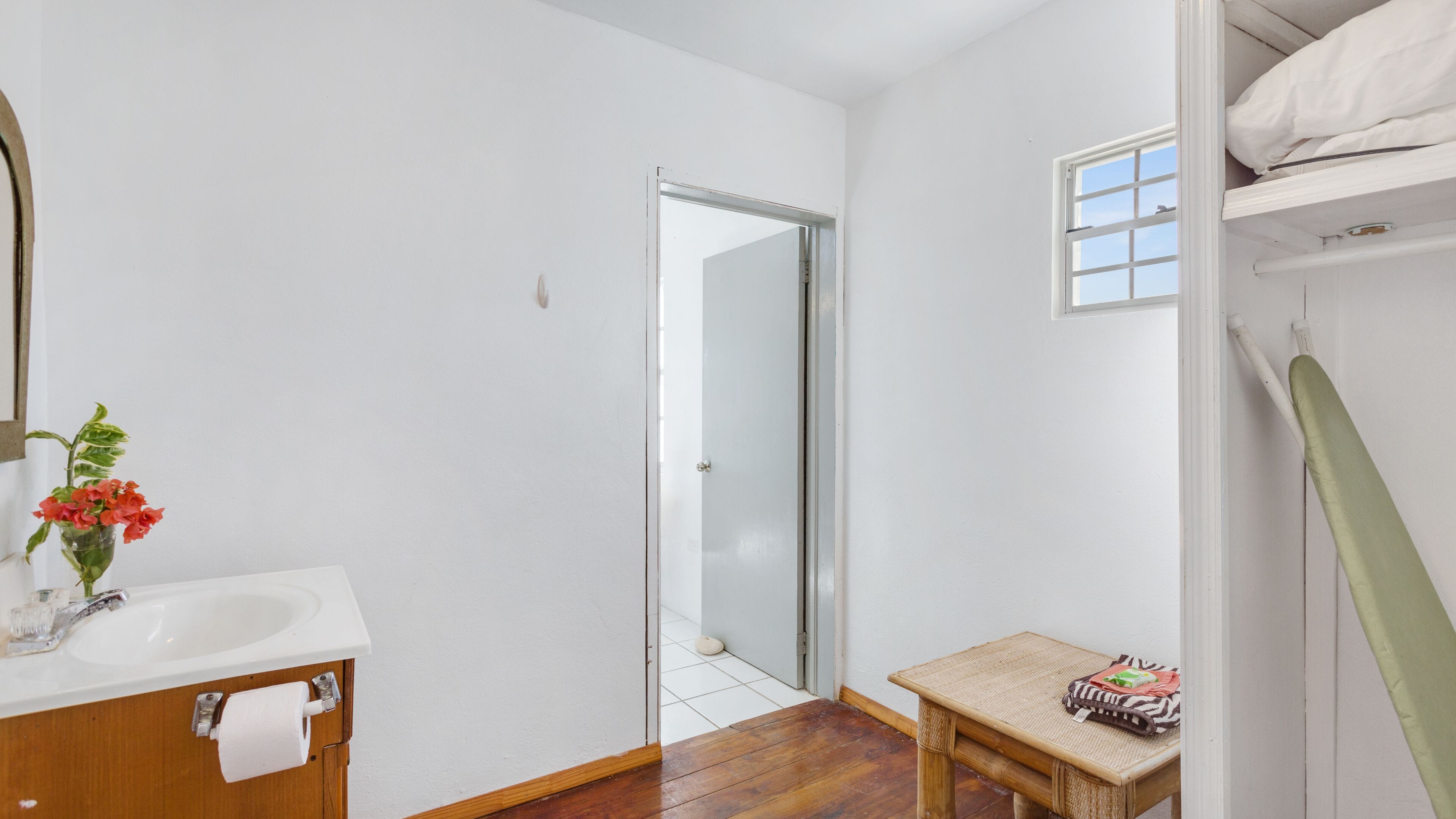 A bathroom with a white sink, a mirror, a small table with a towel, and a shower area.