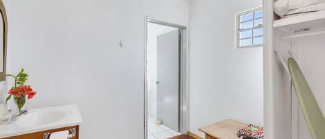 A bathroom with a white sink, a mirror, a small table with a towel, and a shower area.