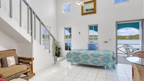 Amplia habitación con cama, sofá, escalera y balcón con vista al agua.