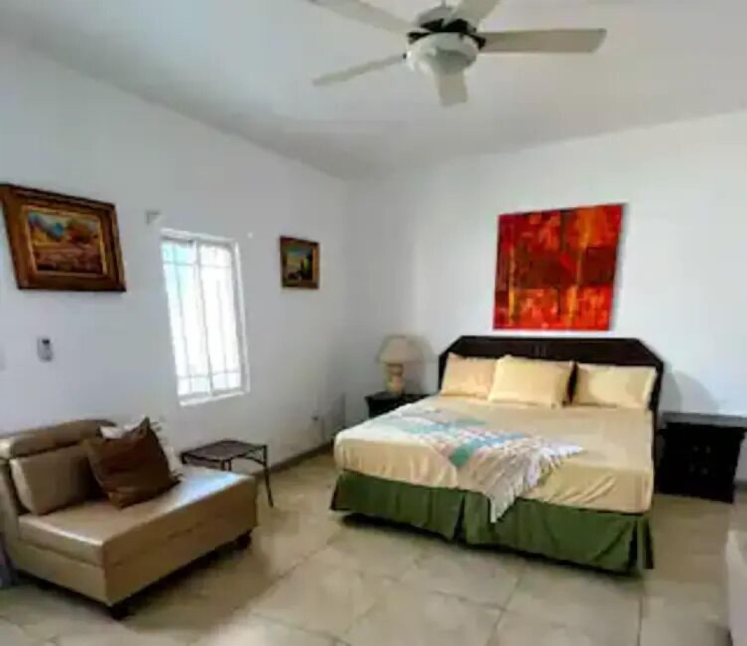A bedroom with a bed, a sofa, a ceiling fan, and artwork on the walls.
