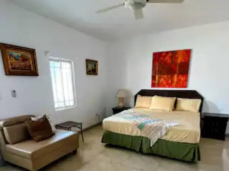 Un dormitorio con una cama, un sofá, un ventilador de techo y obras de arte en las paredes.