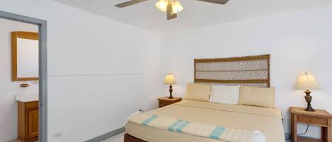 A bedroom with a bed, two bedside tables with lamps, a ceiling fan, a mirror, and a wall-mounted decorative headboard.