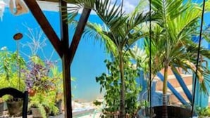 Un espacio al aire libre techado con vigas de madera, plantas en macetas y vista a la playa.