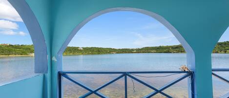 Una habitación con vista a un lago, una barandilla azul y un cojín a rayas.