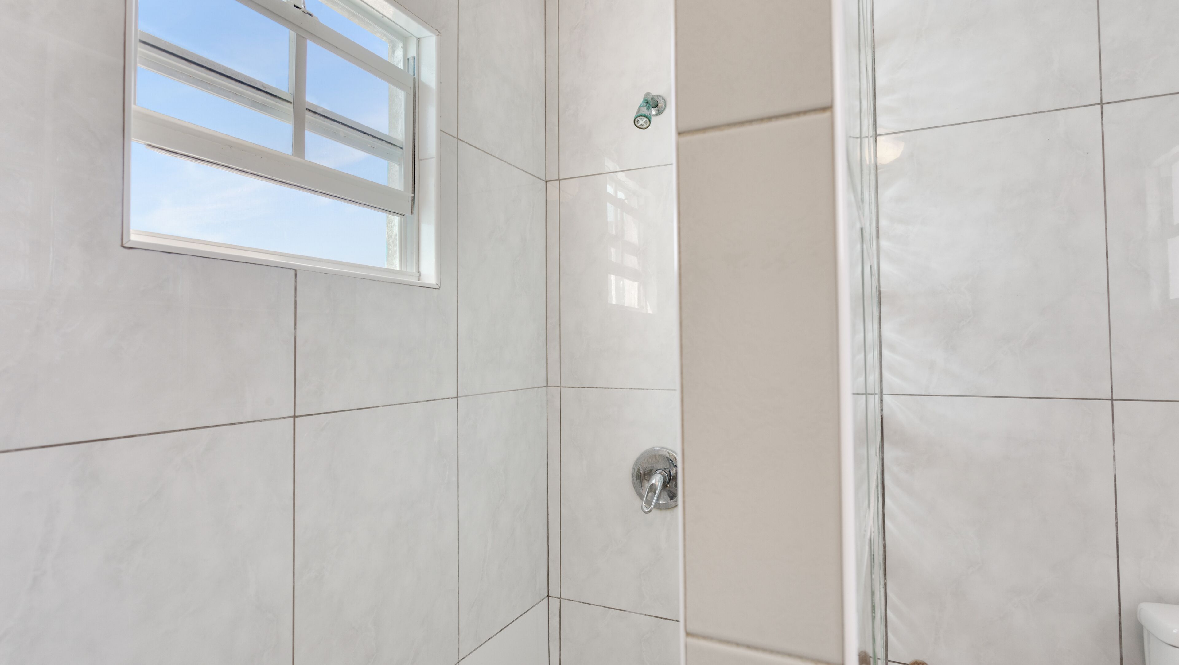 A bathroom with white tiles, a window, and a shower area.