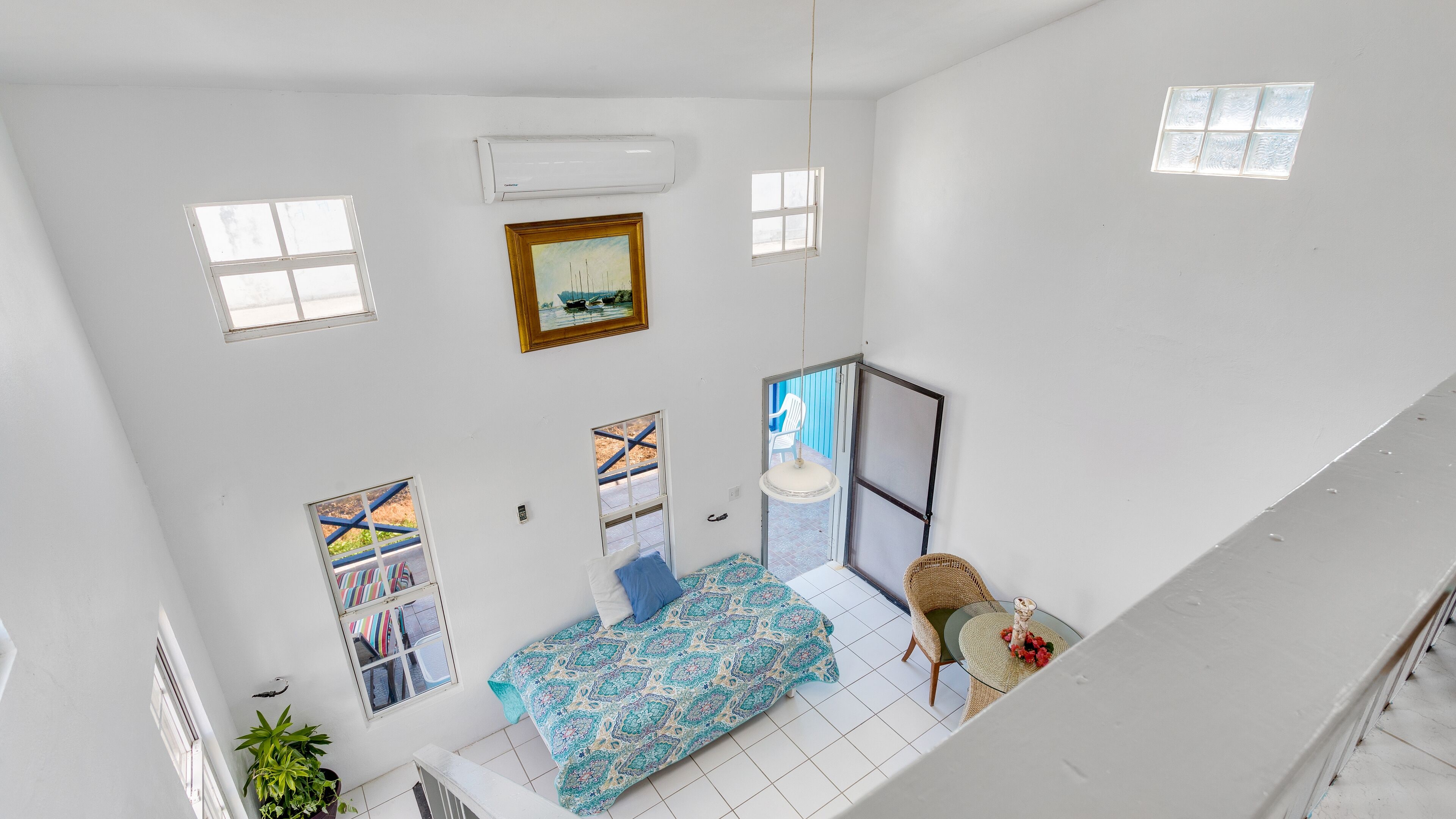 A high-ceiling room with a bed, a chair, a small table, and a window.