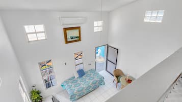 A high-ceiling room with a bed, a chair, a small table, and a window.