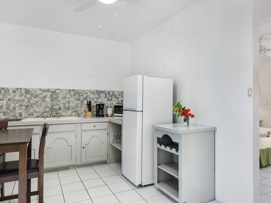 A compact kitchen with a white refrigerator, a tiled backsplash, and a dining area with a wooden table and chairs.