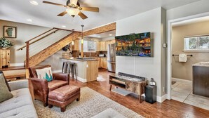 A spacious living area with a wooden staircase, a kitchen with a large island, and a ceiling fan. - Dancing Bear Cabin Pet Friendly, Sleeps 4, Totally Cute! (South Lake Tahoe)