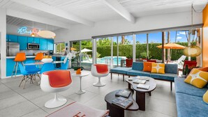 A modern kitchen with blue cabinets, a dining area with orange chairs, and a living room with a blue sofa and orange cushions. - Mid-Century Alexander Pool Home Featured in Modernism Week (Palm Springs)