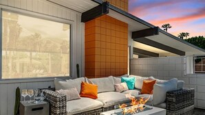 An outdoor seating area with a fire feature, a cushioned sofa, and a side table with glasses. - Mid-Century Alexander Pool Home Featured in Modernism Week (Palm Springs)