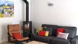 Ein Wohnzimmer mit einer Couch, einem Sessel, einem Holztisch und einem schwarzen Kaminofen.