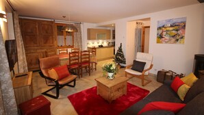 Ein Wohnzimmer mit einer Couch, Sesseln, einem Couchtisch, einem Kamin und einer Küche im Hintergrund.