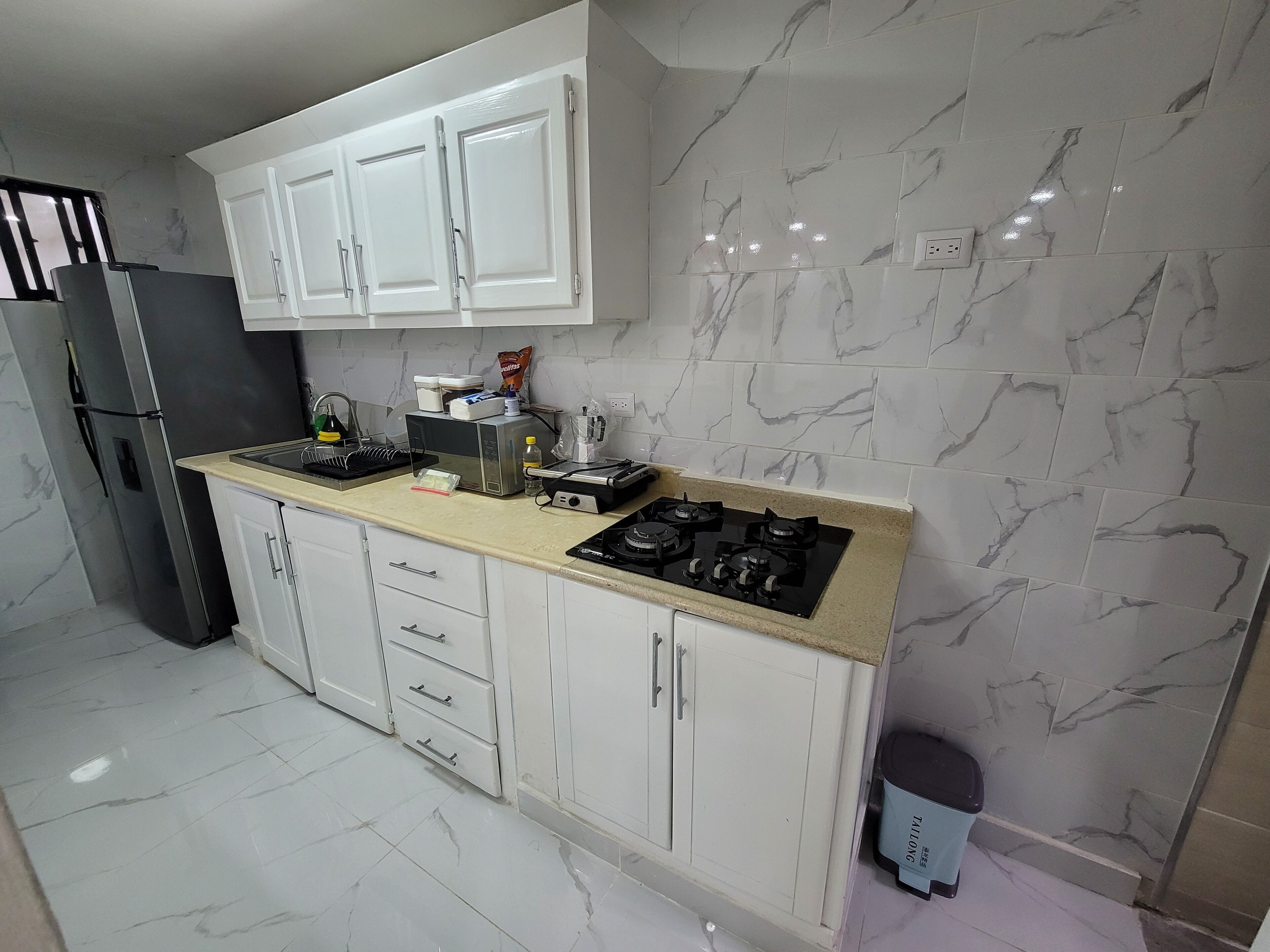 Une cuisine avec des meubles blancs, un réfrigérateur noir, une cuisinière à gaz et des murs à motifs de marbre.