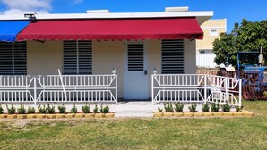A two-story building with a red awning, white railings, and a small garden area with plants. - Beachfront Studios (Fajardo)