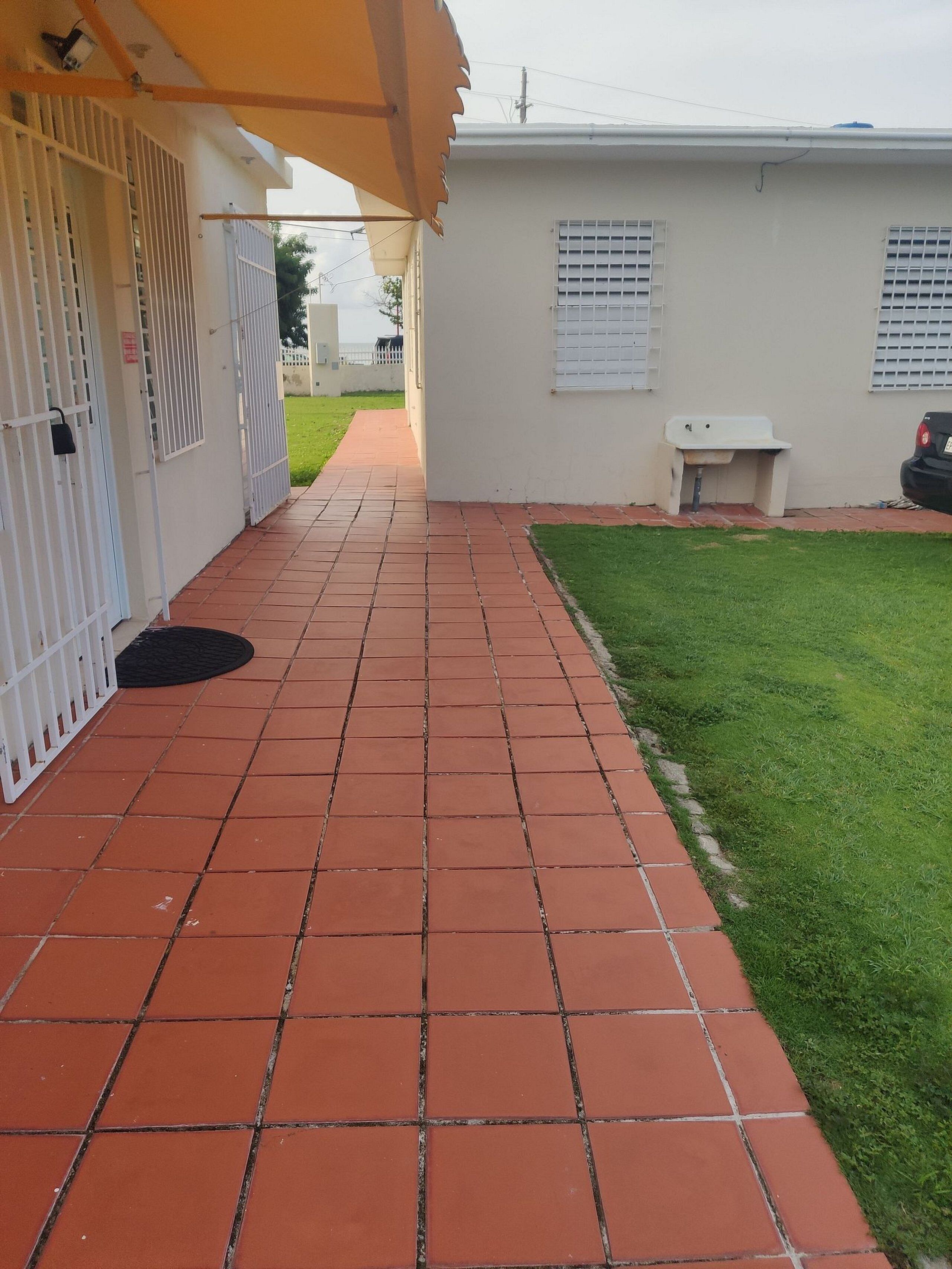 A paved walkway leading to a building with a white exterior and a small sink area.