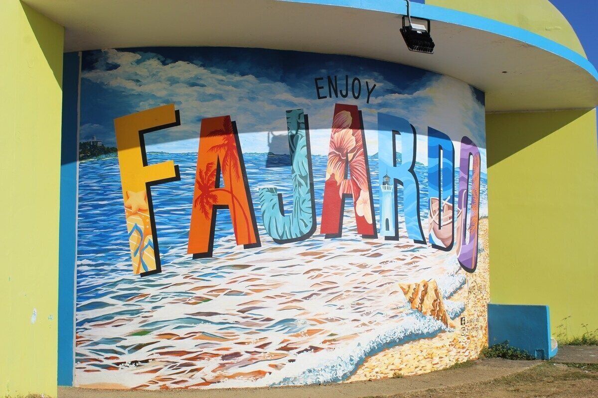A mural with the word 'FAJARDO' and 'ENJOY' on a curved wall, depicting a beach scene with waves and palm trees.