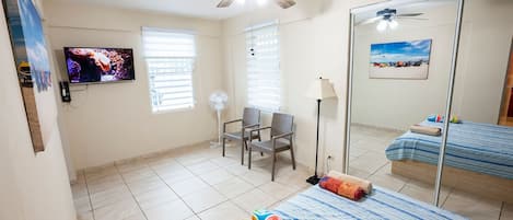 A hotel room with a bed, a chair, a TV, a ceiling fan, and a window with blinds.