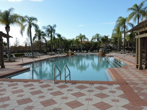 Una piscina con solárium de baldosas, palmeras y sillas de descanso.