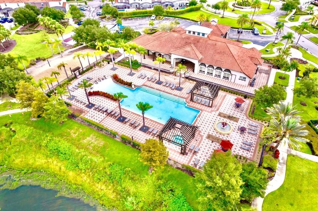 An aerial view of a resort with a swimming pool, lounge areas, and a large building with a tiled roof.