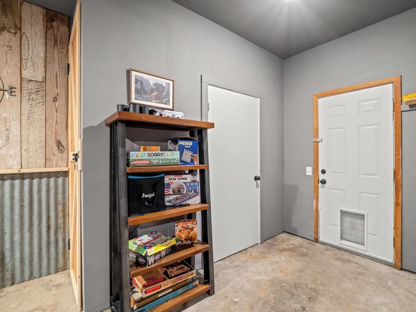 A room with a wooden shelf holding board games, a white door, and a wooden wall panel.