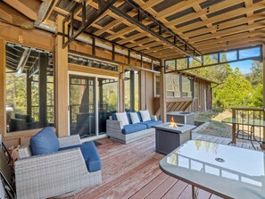A covered outdoor seating area with wicker furniture, a glass table, and a fire feature.