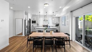 Een moderne keuken met een centraal eiland, roestvrijstalen apparatuur en een eethoek met een houten tafel en stoelen.
