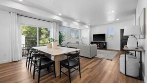 Een moderne woonkamer met een eethoek, een bank, een televisie en een balkon met gordijnen.