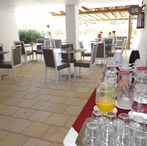 Una zona de dinar amb taules i cadires, una barra de menjar amb aliments i begudes, i una zona d'estar a l'aire lliure coberta.
