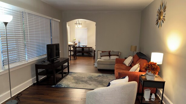A living room with a sofa, armchair, TV, and a dining area with a table and chairs.