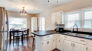 A kitchen with white cabinets, a black countertop, a stainless steel refrigerator, and a dining area with wooden chairs.