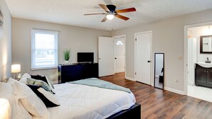 A bedroom with a bed, a ceiling fan, a dresser, a TV, a window, and a door.