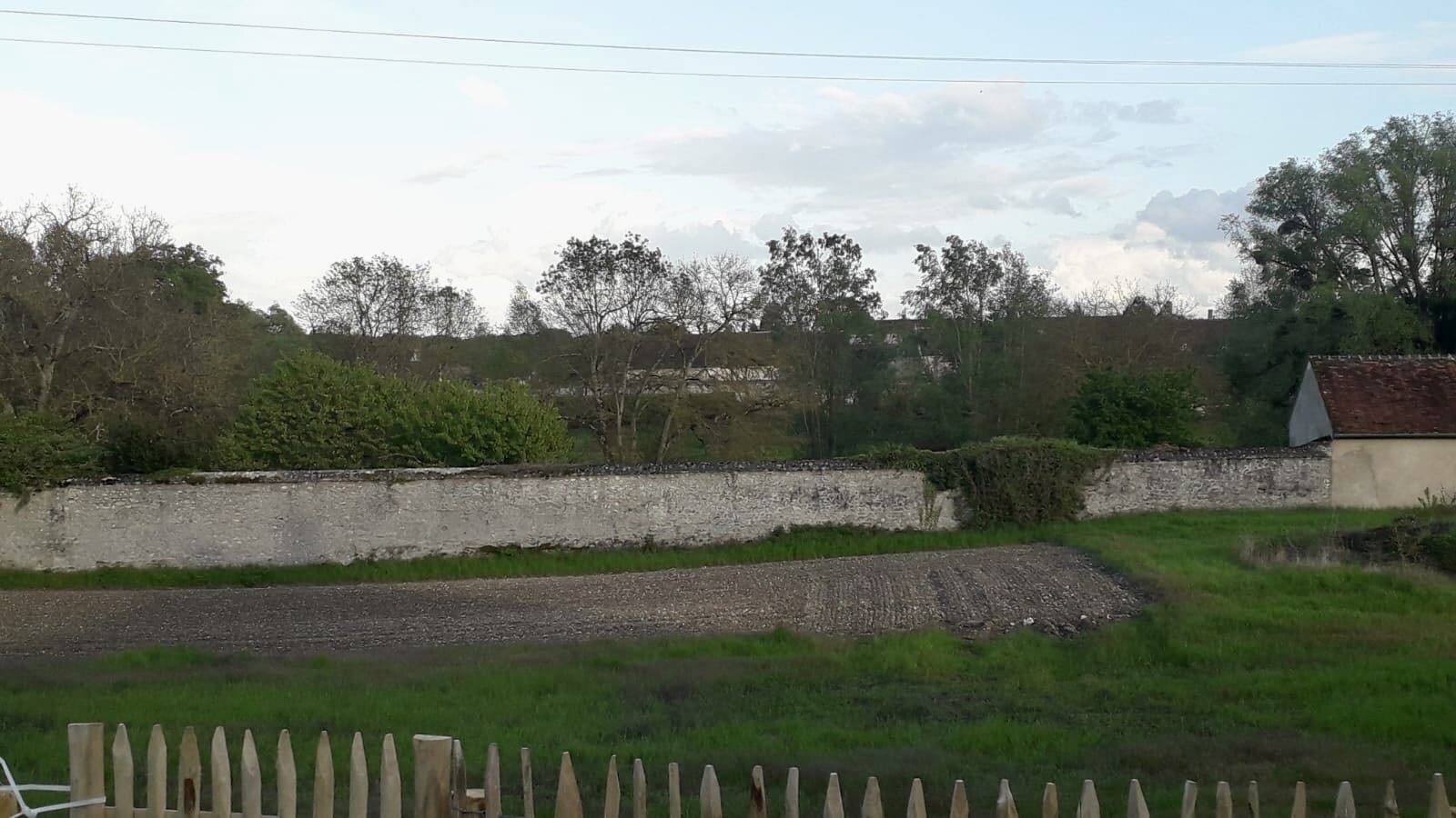 Un paysage rural avec un mur de pierres, un chemin de gravier et une clôture en bois.
