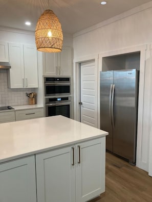 A modern kitchen with white cabinetry, a stainless steel refrigerator, and a hanging light fixture.