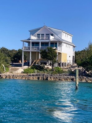 A two-story waterfront property with a balcony, a covered porch, and a view of the water.