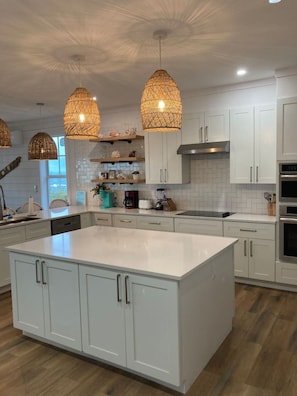 Una cocina moderna con armarios blancos, una isla grande, luces colgantes y una estufa a la vista.