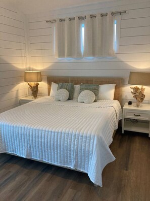 A bedroom with a large bed, two bedside tables, a headboard, and a window with curtains.