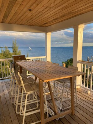 A wooden deck with a table and chairs, overlooking a body of water with a boat in the distance.