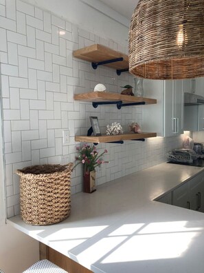 A modern kitchen with white herringbone tile backsplash, wooden floating shelves, and a woven basket.