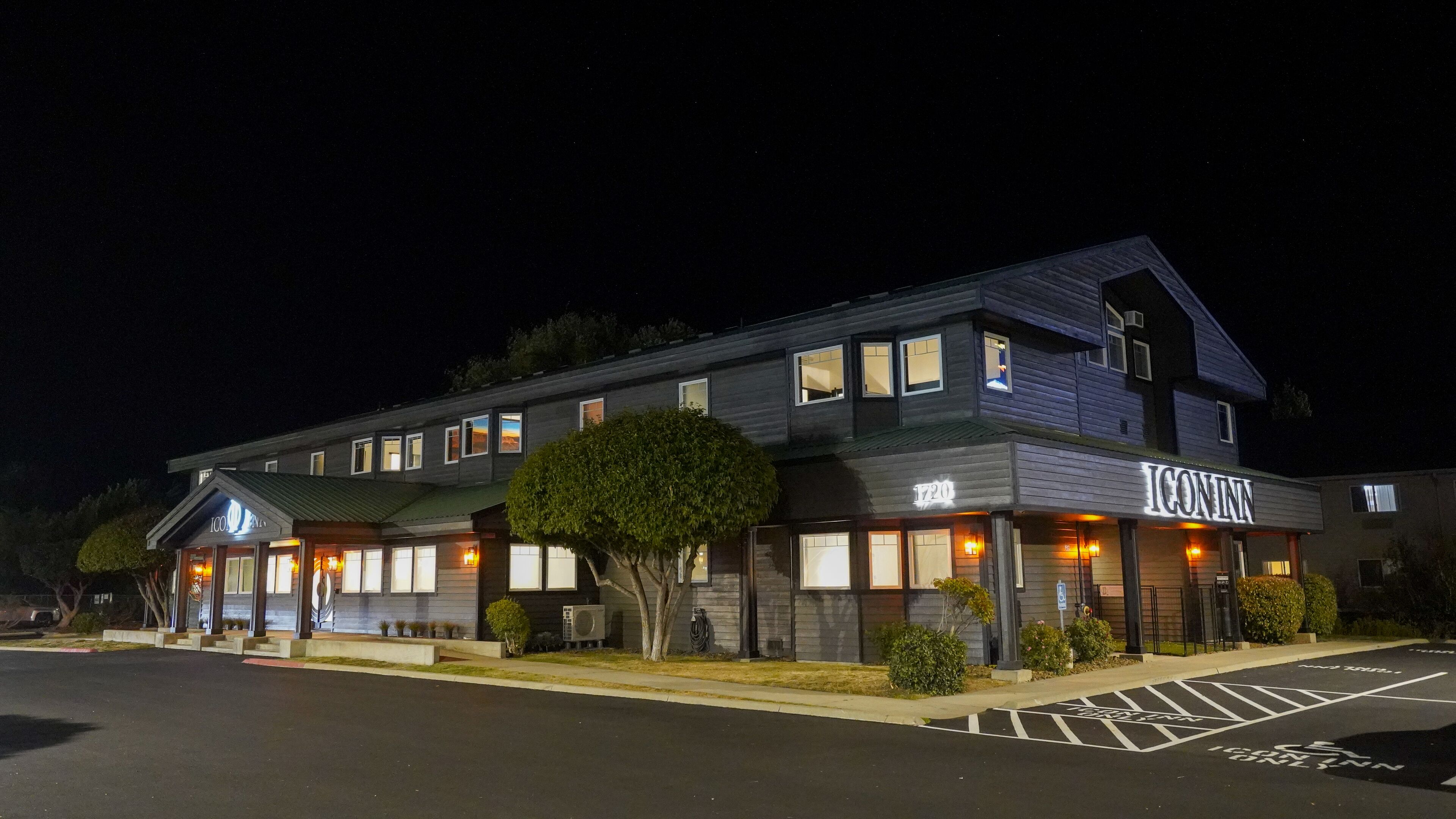 A two-story hotel with a dark facade, illuminated windows, and a sign reading "ICONINN".