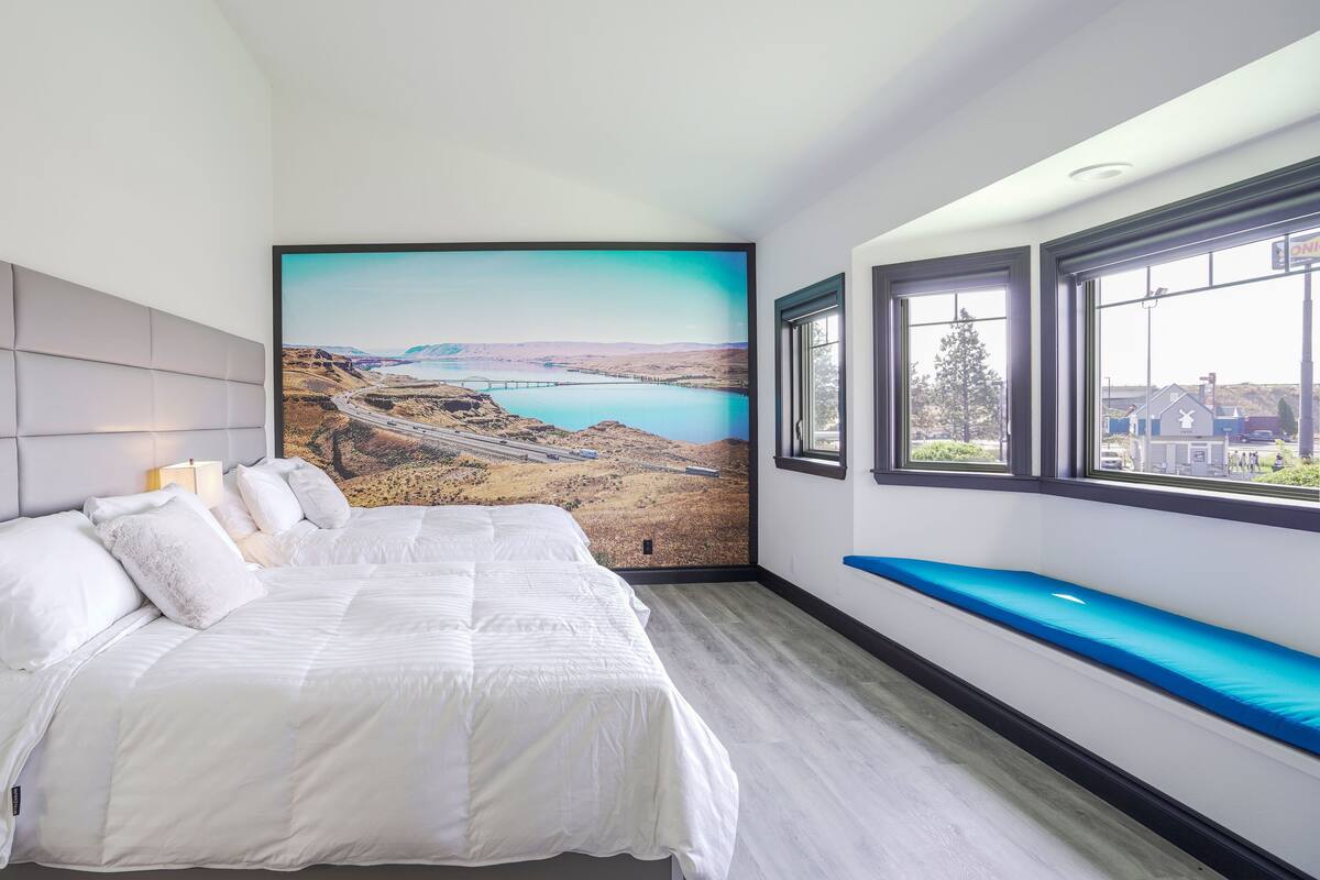 A bedroom with a bed, a headboard, a window with a view of a landscape, and a wall with a large picture.