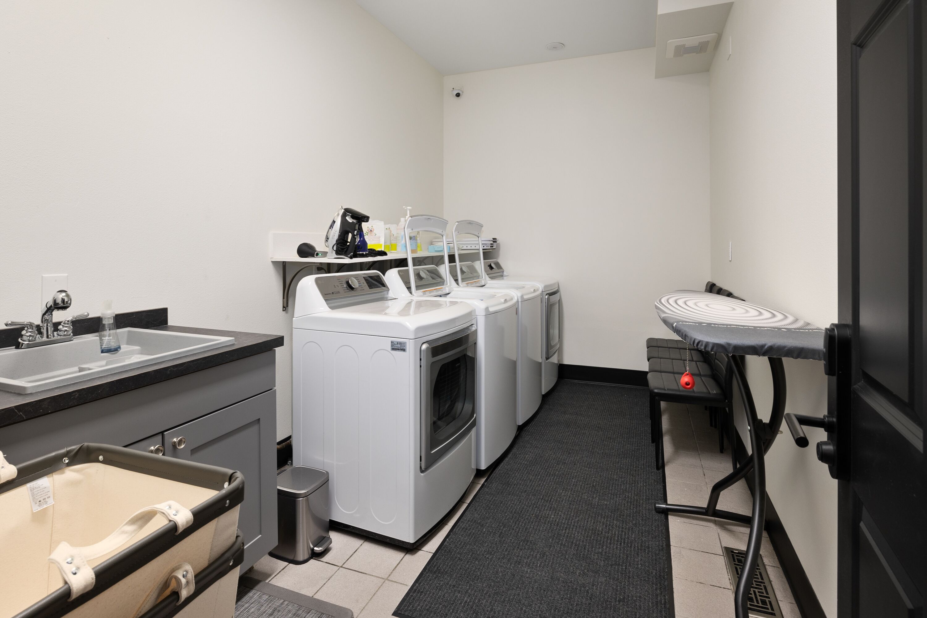 A laundry room with a sink, washing machines, and a drying station.