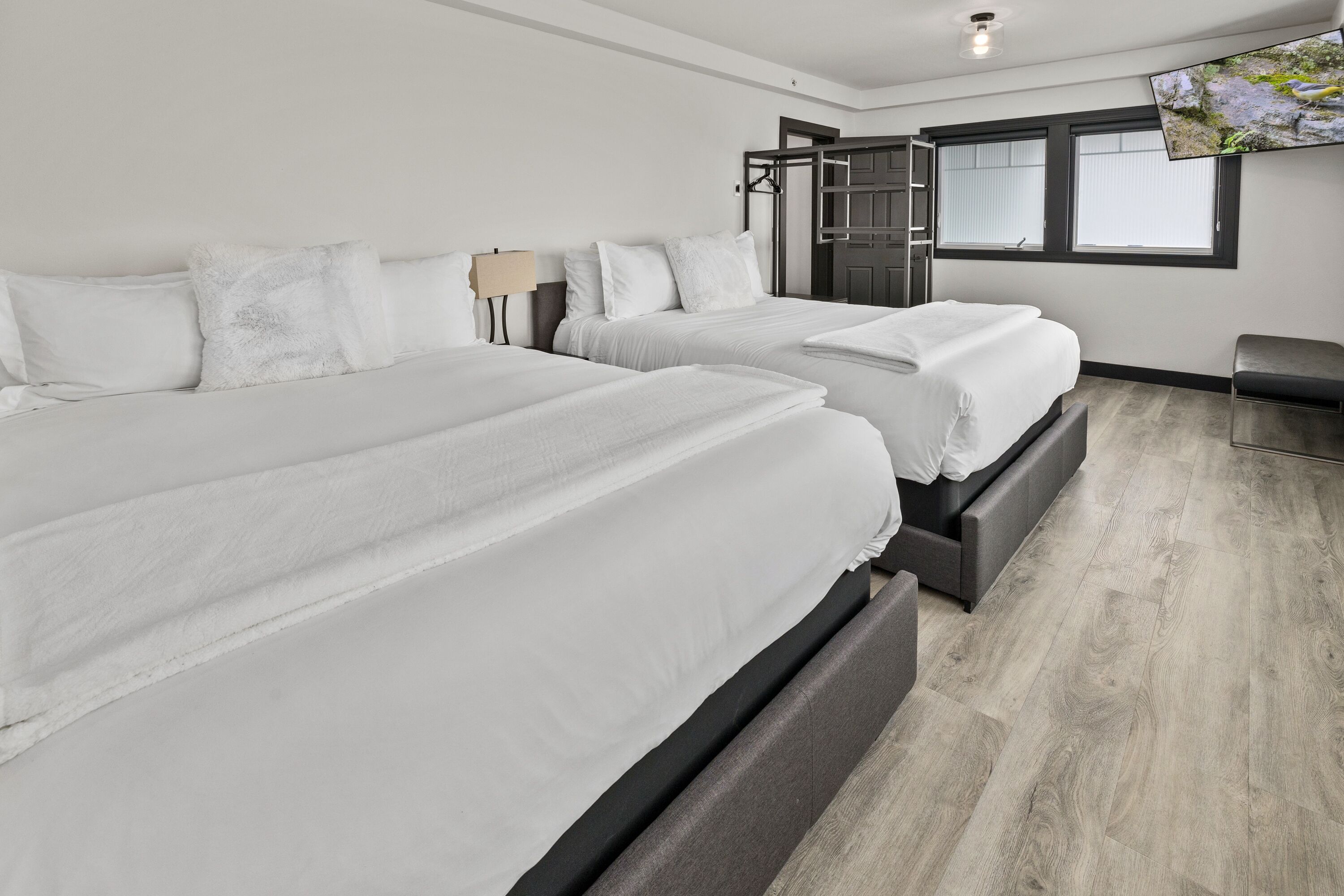 Ein modernes Hotelzimmer mit zwei Betten, einem an der Wand befestigten Fernseher und einem Fenster mit Jalousien.