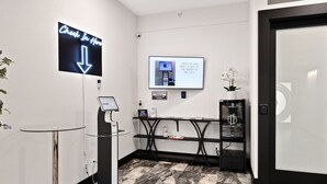 A reception area with a digital sign directing to the chest in the hallway, a kiosk for check-in, and a small table with a potted orchid. - Icon Inn (Ellensburg)